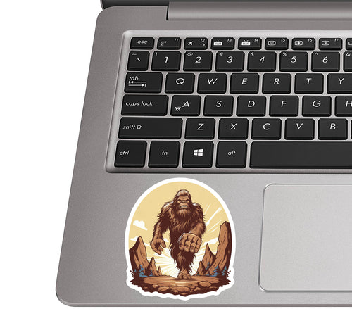 Bigfoot-horizon sticker stuck to a silver laptop palm rest beside a QWERTY keyboard to show sticker dimensions