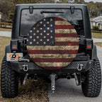 Rustic American flag spare tire cover on red Jeep Wrangler with desert backdrop featuring weathered patriotic design