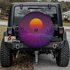 the rear of a black Jeep Wrangler with a large, colorful wheel cover featuring a sunset and mountains.