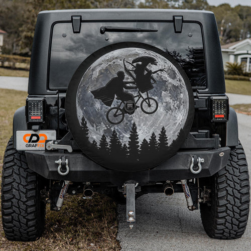 a black Jeep Wrangler with a large tire cover on the rear of the vehicle. The cover depicts a silhouetted image of two people riding a bicycle against a backdrop of a full moon and trees.