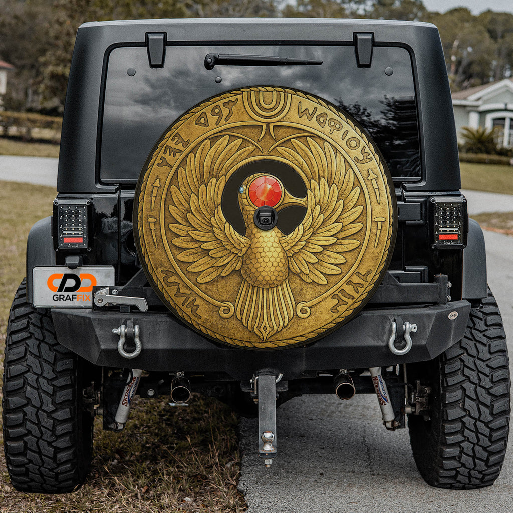a black Jeep Wrangler with a large, ornate gold-colored wheel cover featuring an Egyptian-style bird design.