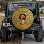 a black Jeep Wrangler with a large, ornate gold-colored wheel cover featuring an Egyptian-style bird design.