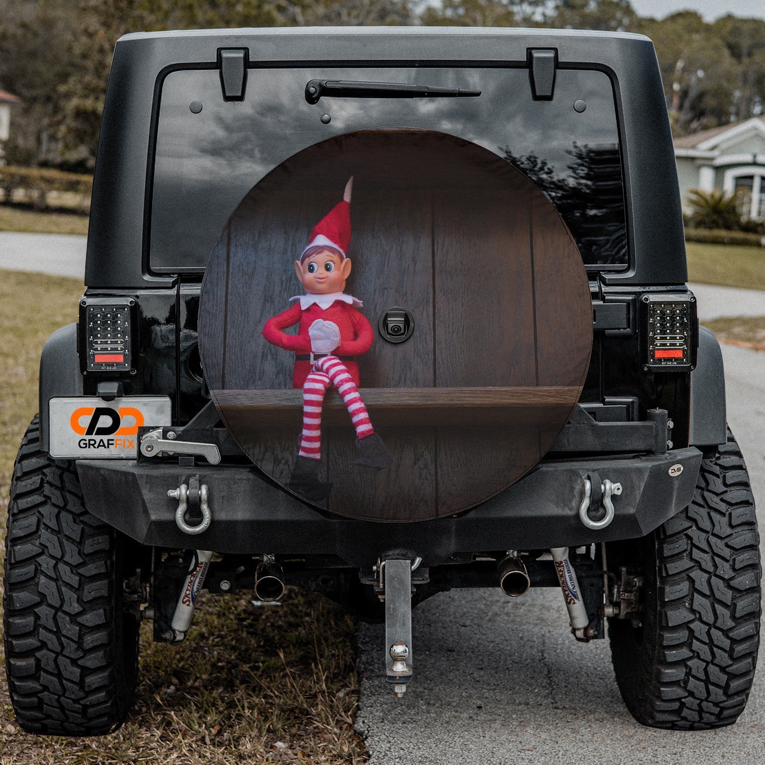 Shelfside Shenanigans spare tire cover mounted on a Jeep rear wheel displaying the festive shelf elf illustration
