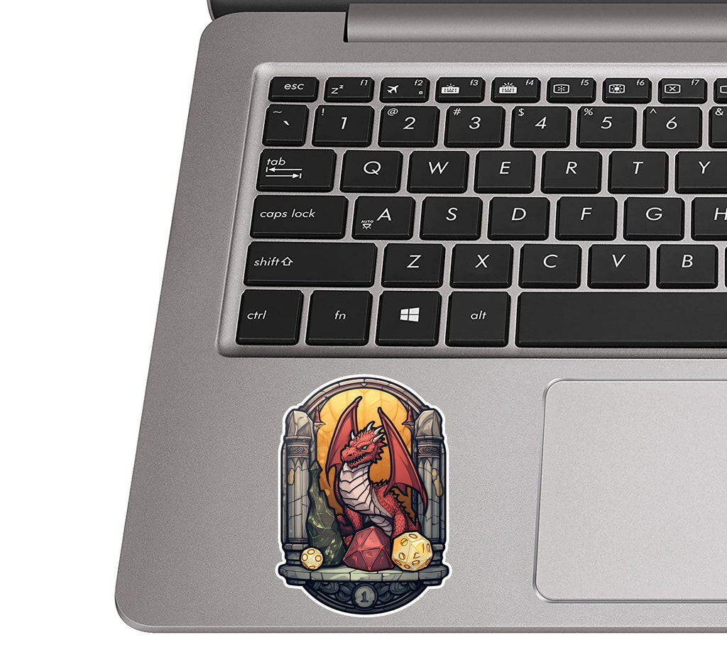Red dragon and D20 decal stuck on a silver laptop palm rest beside a black QWERTY keyboard for true size feel