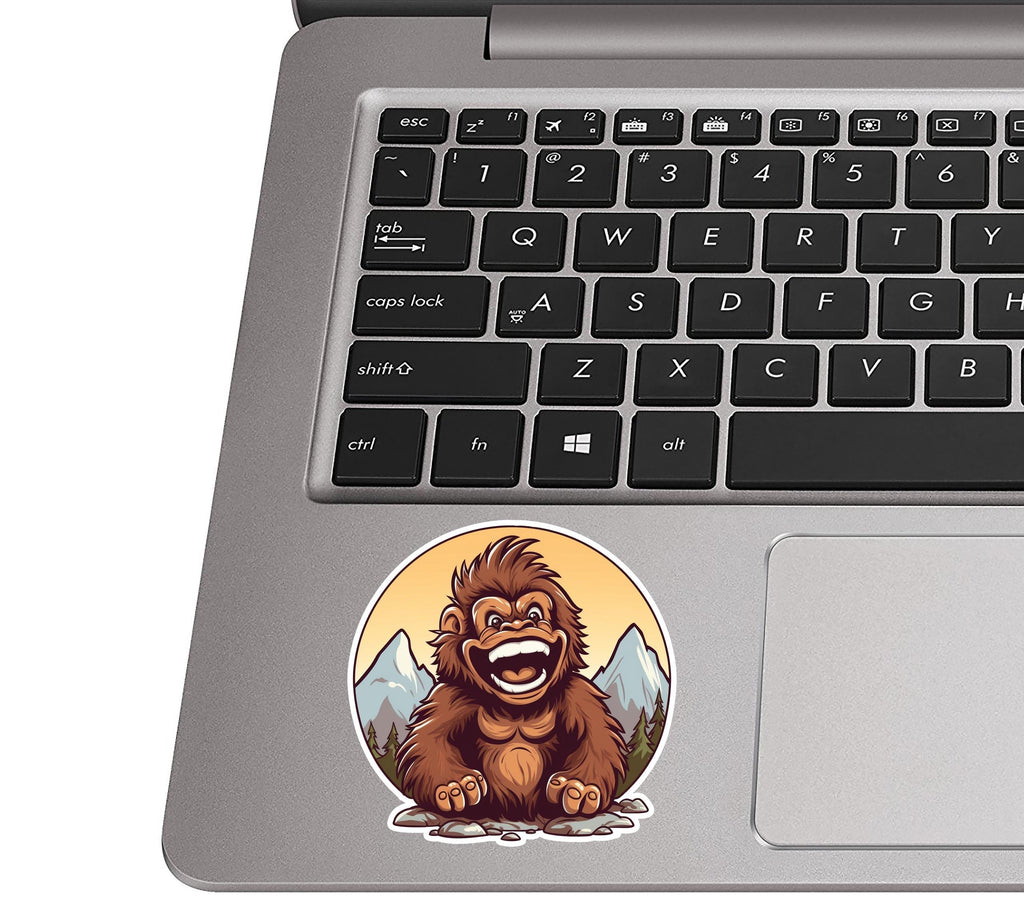 Smiling baby sasquatch sticker on a silver laptop palm rest near a black QWERTY keyboard for size context