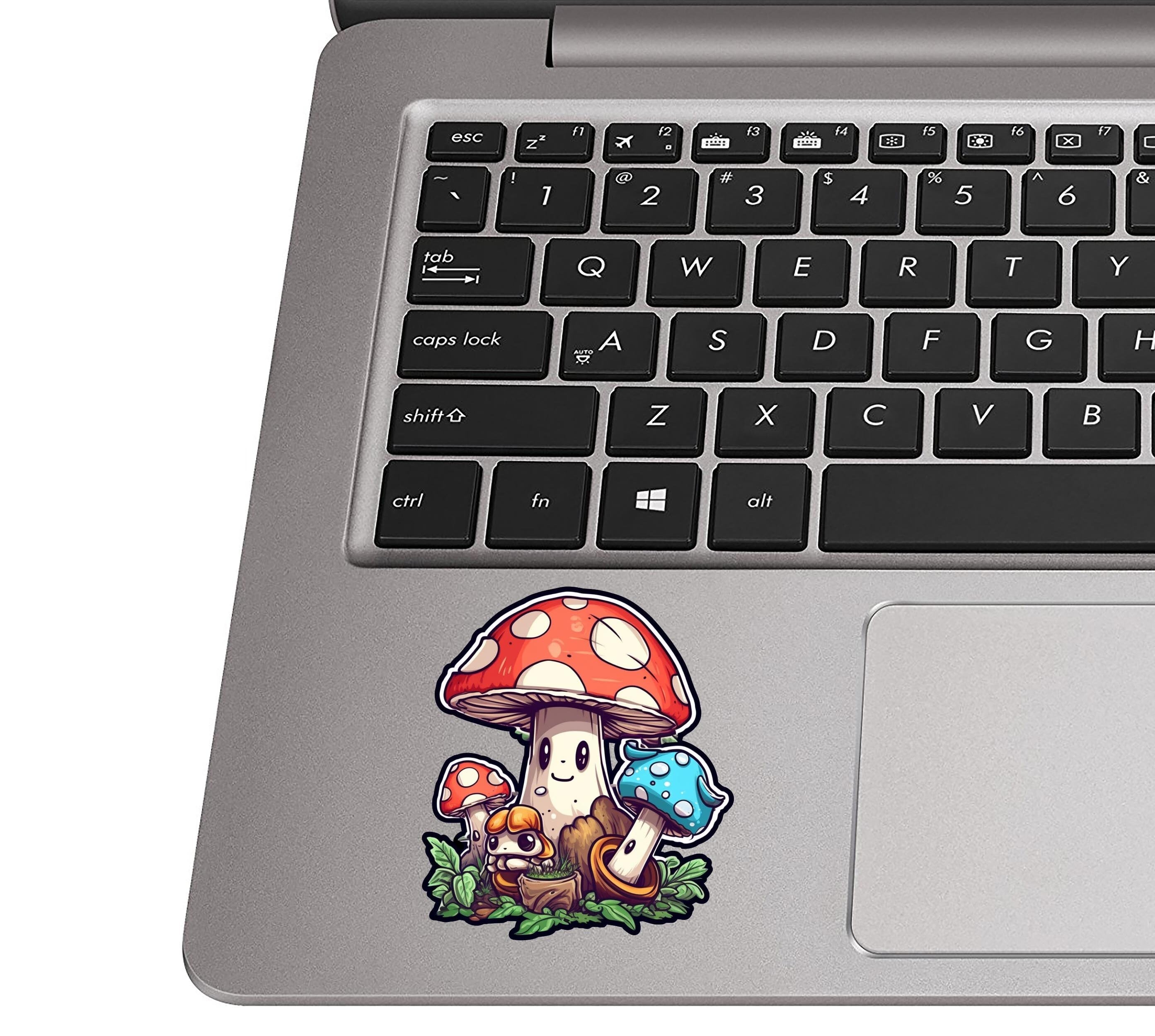 Happy mushroom family sticker on a silver laptop palm rest near a black QWERTY keyboard for sizing