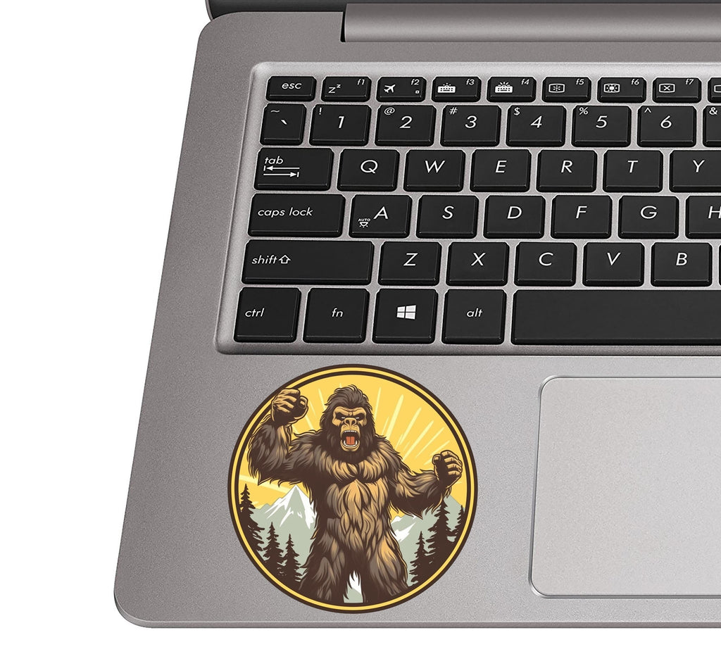 Roaring angry sasquatch sticker on a silver laptop palm rest near a black QWERTY keyboard for size context