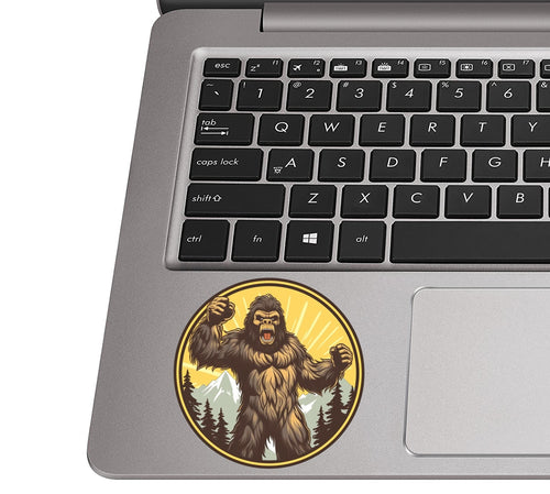Roaring angry sasquatch sticker on a silver laptop palm rest near a black QWERTY keyboard for size context