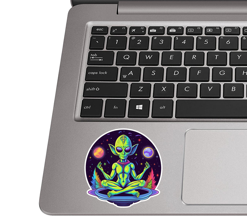 Psychedelic meditating alien sticker on a silver laptop palm rest near a black QWERTY keyboard for size scale
