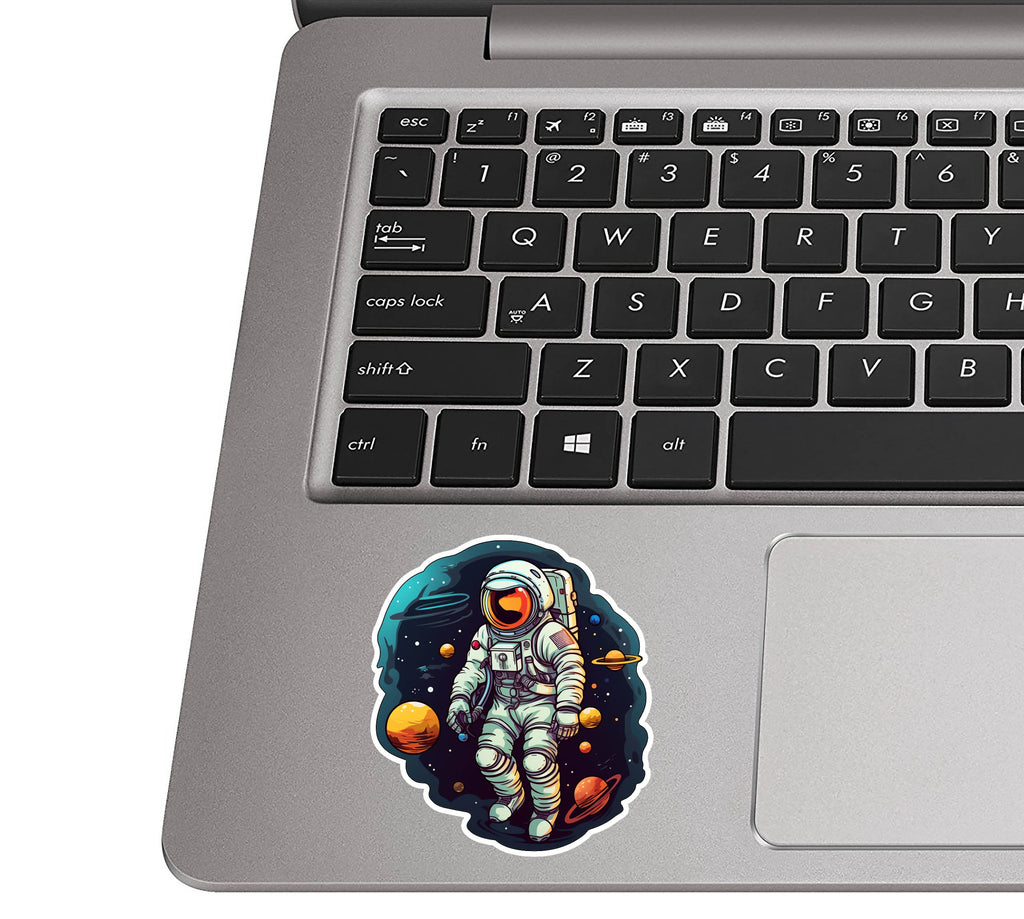 Sci-fi astronaut vinyl sticker on a silver laptop palm rest beside a black QWERTY keyboard for size scale
