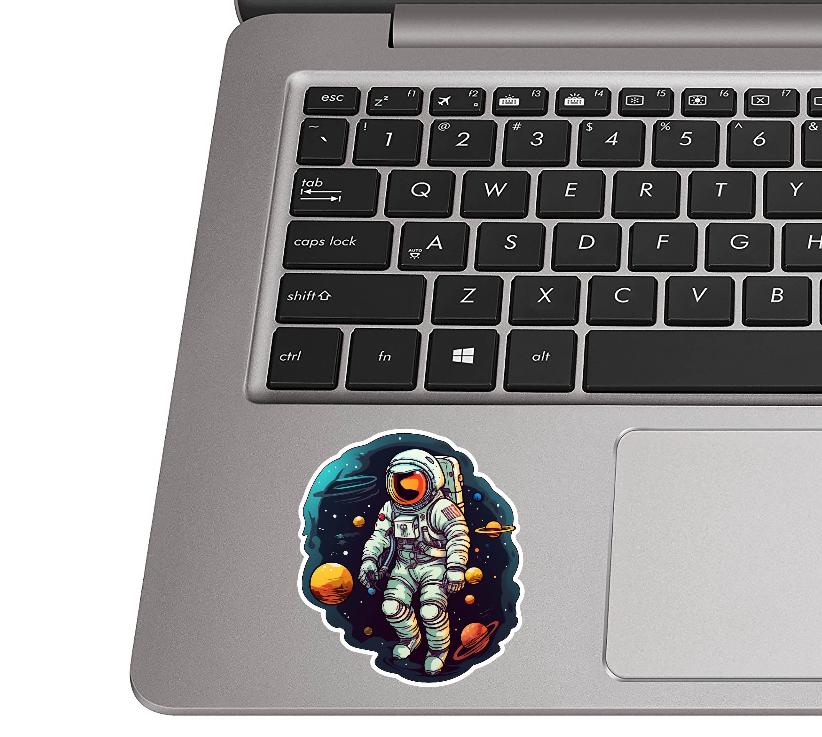 Sci-fi astronaut vinyl sticker on a silver laptop palm rest beside a black QWERTY keyboard for size scale
