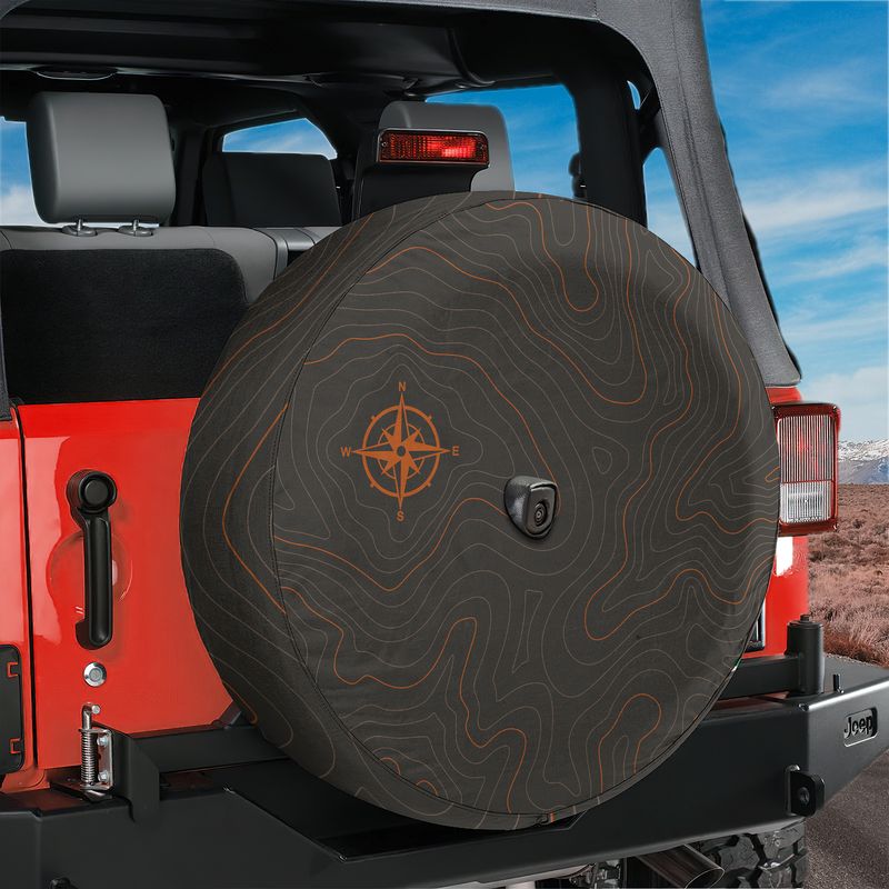 Topographic map tire cover on black Jeep Wrangler showing orange topo contour lines and compass design